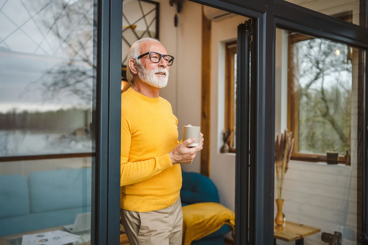 Man met een kop koffie in de deuropening van een woning aan het water