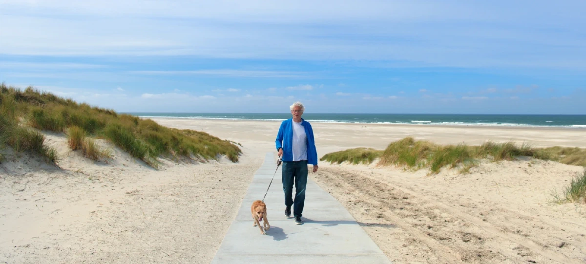Oudere man laat hond uit op het strand