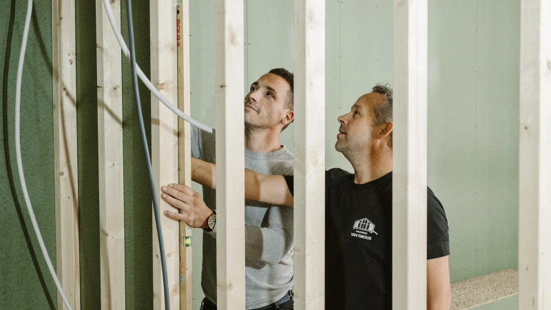 Twee bouwers van Van Emous plaatsen een binnenwand in het houtskelet van een woning
