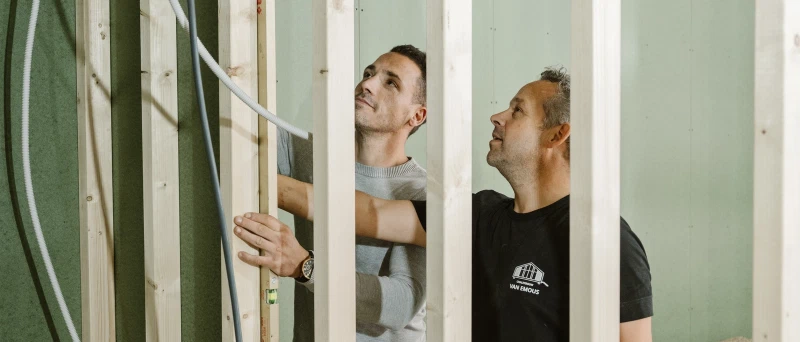Twee bouwers van Van Emous plaatsen een binnenwand in het houtskelet van een woning