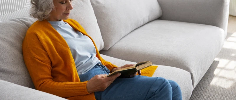 Oudere vrouw leest ontspannen op de bank in haar woning