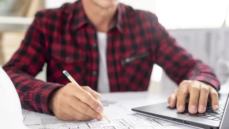 Man werkt aan bouwtekeningen achter een laptop