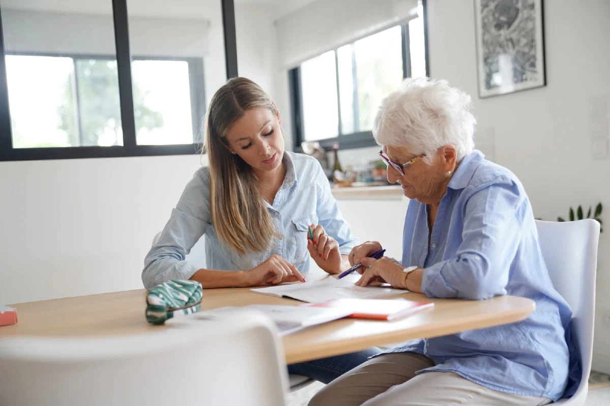 Vrouw helpt oudere moeder met het invullen van papierwerk aan tafel